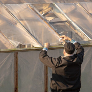 Worker repairs a damaged greenhouse cover using heavy-duty Greenhouse Material Repair Tape