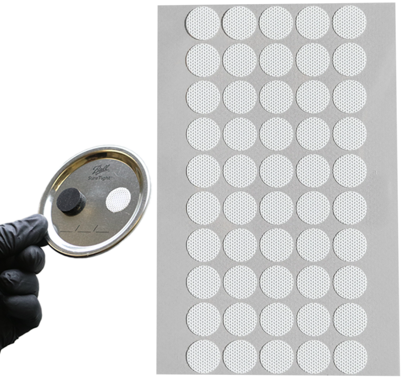 Cultivator holding up a gloved hand with jar lid with self-healing injection port stuck onto it in front of a sheet of the self-healing injection ports.