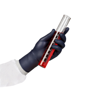 A person's arm in PPE with a black nitrile glove holding a testube with red liquid.