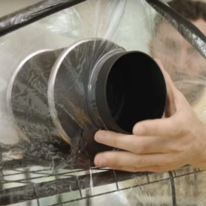 A black inline duct fan being installed in a martha tent for mushroom growing to promote FAE or fresh air exchange.